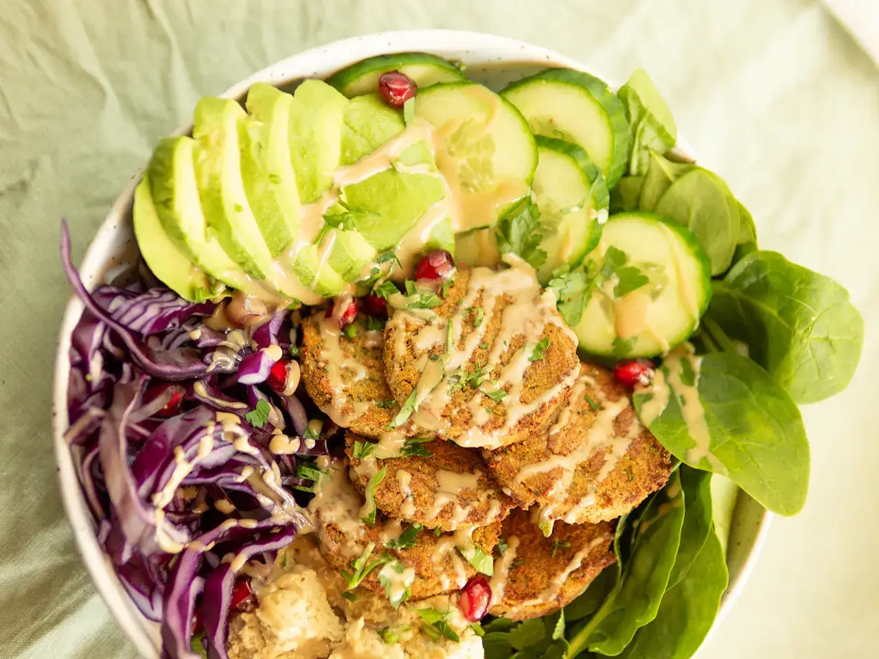 Kolorowy bowl z falafelami, awokado, czerwoną kapustą, og&oacute;rkiem i szpinakiem, polany sosem. Pyszne i zdrowe danie.