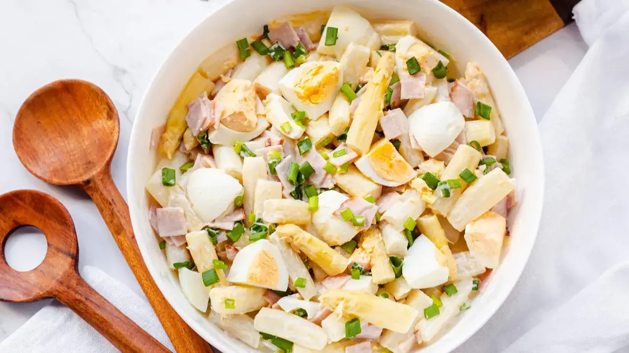 Ein köstlicher Spargelsalat mit Ei, Schinken und Schnittlauch in einer weißen Schüssel, bereit zum Servieren.