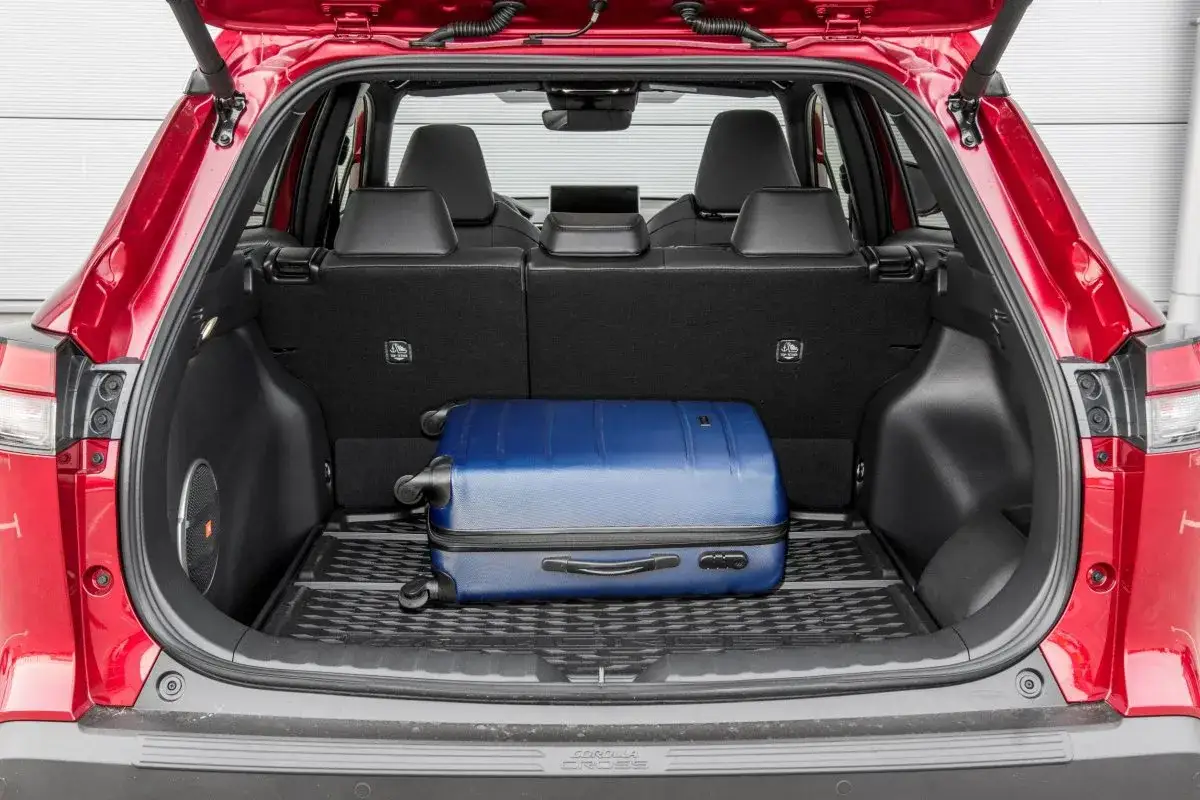 Bagażnik czerwonego Toyota Cross Hybrid mieści niebieską walizkę. Idealny na podróż!