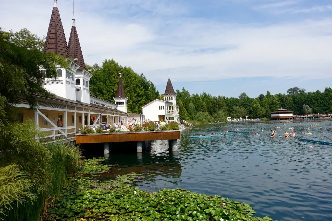 Ein sonniger Tag am Thermalsee in H&eacute;v&iacute;z, Ungarn. Menschen entspannen sich im Wasser, w&auml;hrend im Hintergrund die charakteristischen T&uuml;rme des Badehauses emporragen.