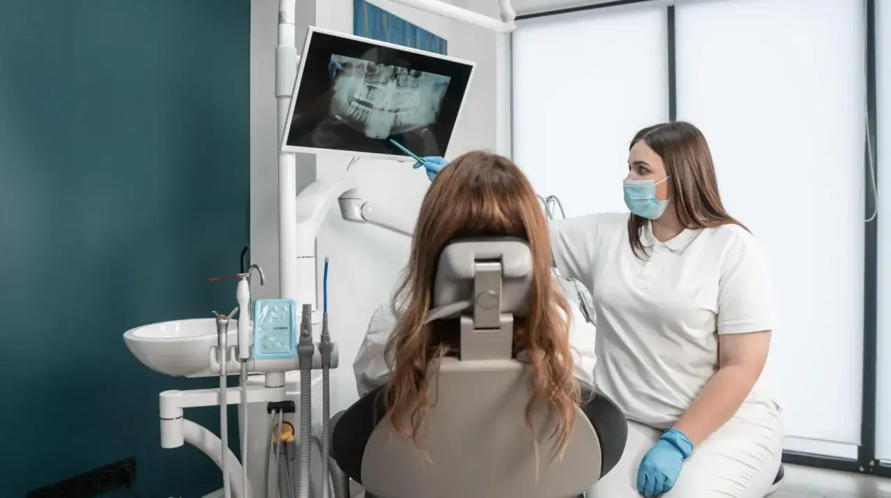 Dentystka pokazuje pacjentce na ekranie rentgen stomatologiczny, omawiając diagnozę.