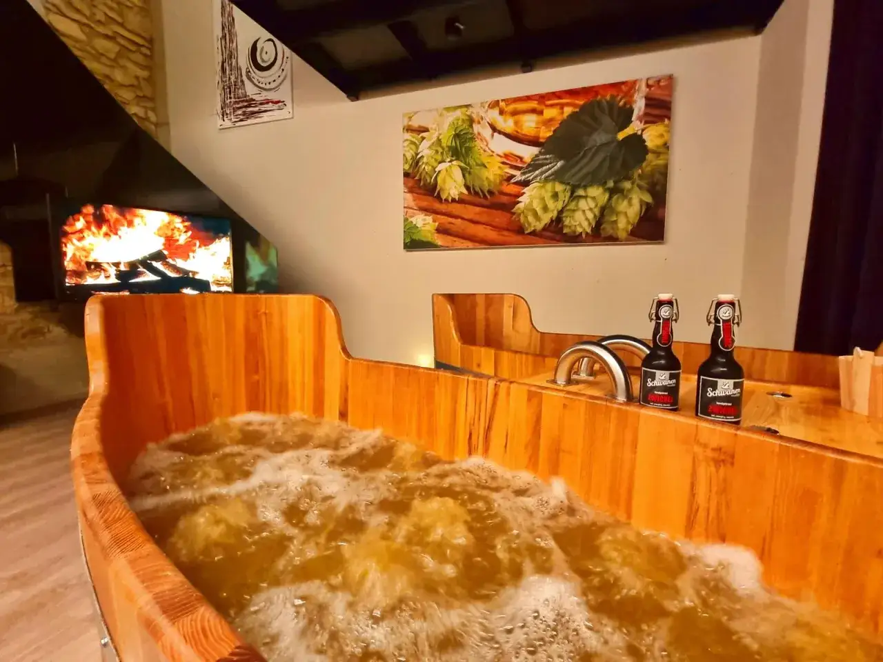 Holzbadewanne gef&uuml;llt mit sprudelndem Bier, bereit f&uuml;r ein entspannendes Bier-Spa-Erlebnis. Zwei Bierflaschen stehen bereit.