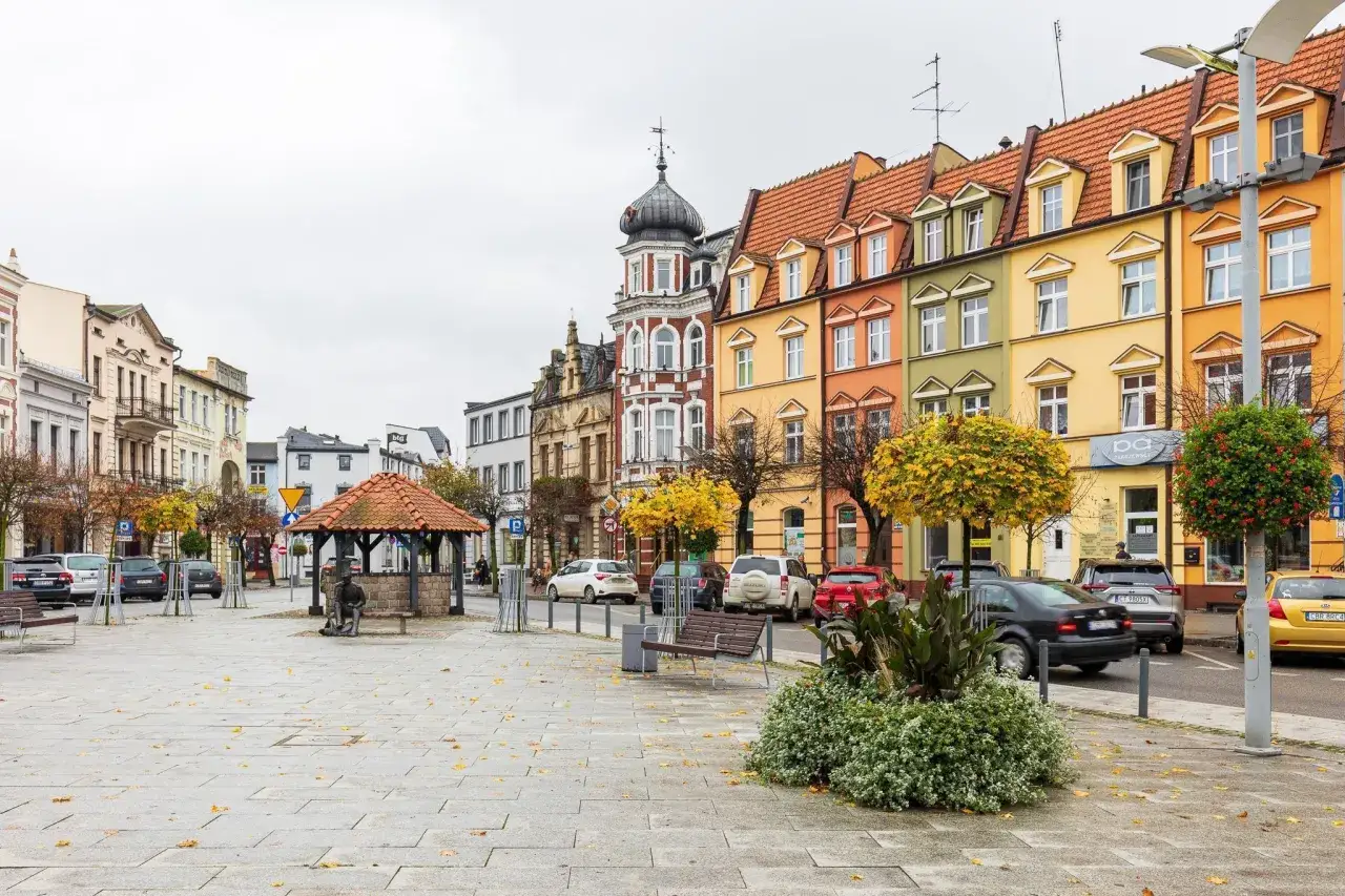 Kolorowy brodnica rynek z kamienicami, studnią i ławkami. Jesienne liście na bruku.