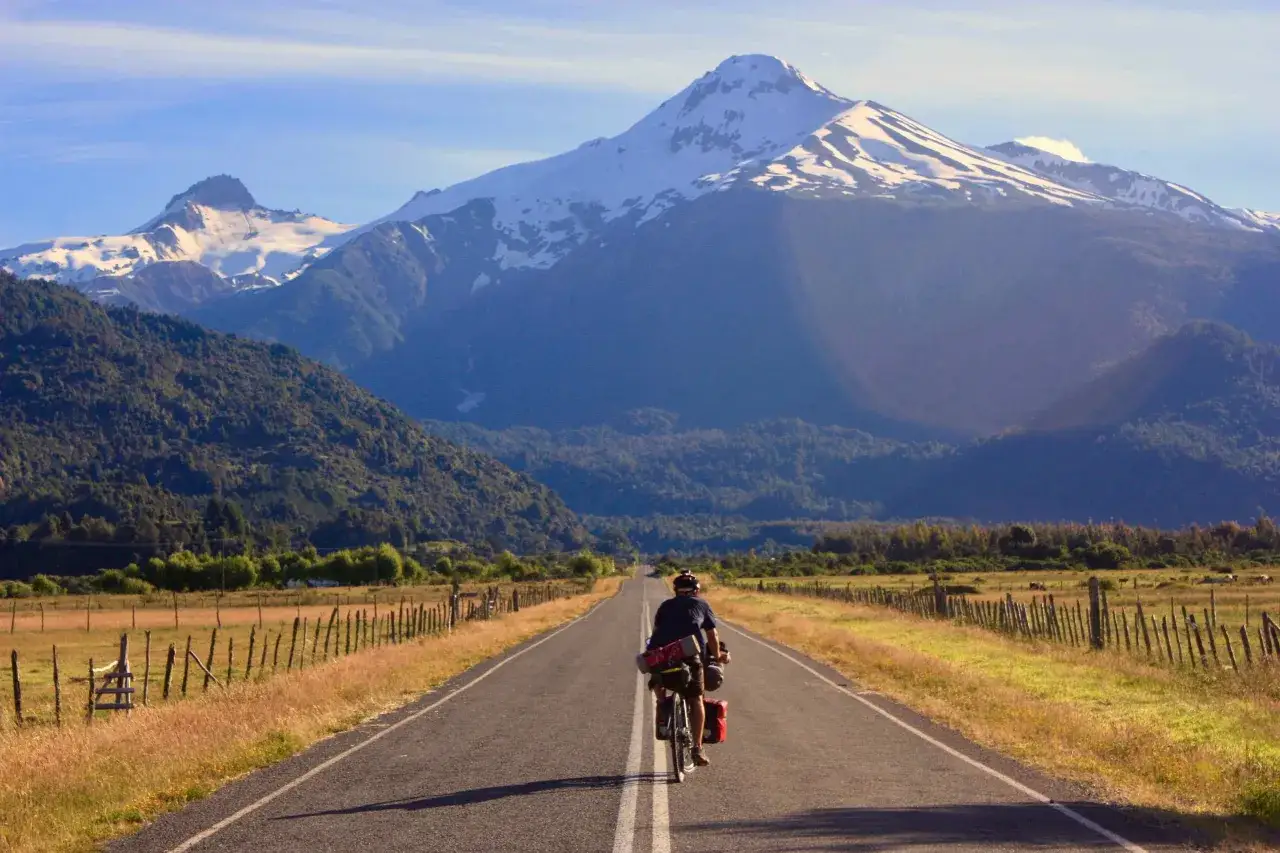 Ciclista pedaleando por la Carretera Austral, con imponentes monta&ntilde;as nevadas de fondo.