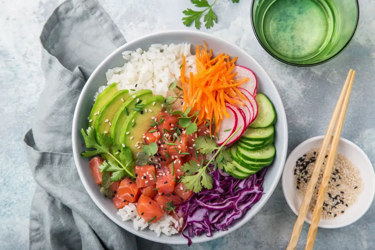 Kolorowy Poke Bowl przepis: ryż, łosoś, awokado, marchewka, rzodkiewka, ogórek, czerwona kapusta i sezam.