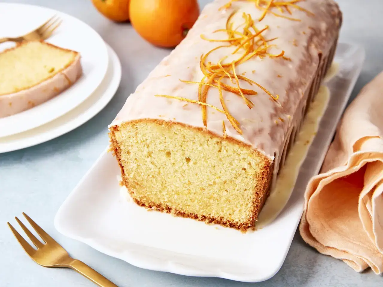 Omas saftiger Orangenkuchen mit Zuckerguss und Orangenzesten, serviert auf einem wei&szlig;en Teller mit einer goldenen Gabel.