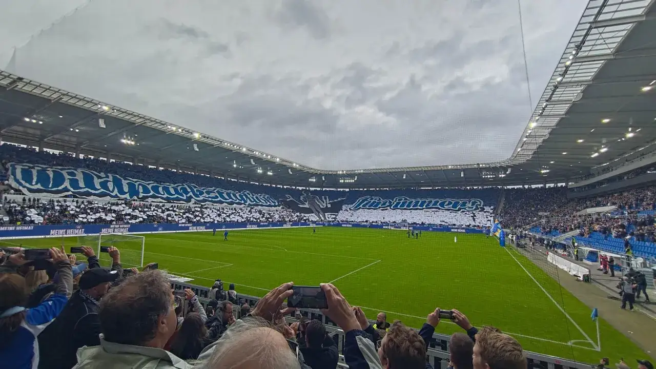 Trybuny stadionu wypełnione kibicami Karlsruher SC, tworzącymi ogromną mozaikę i transparenty.