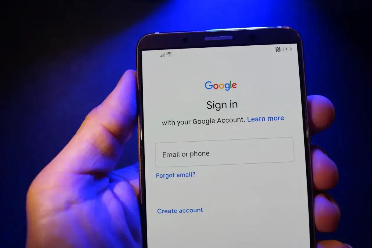 Dłoń trzyma smartfon, na ekranie którego widnieje strona logowania do poczty Gmail.