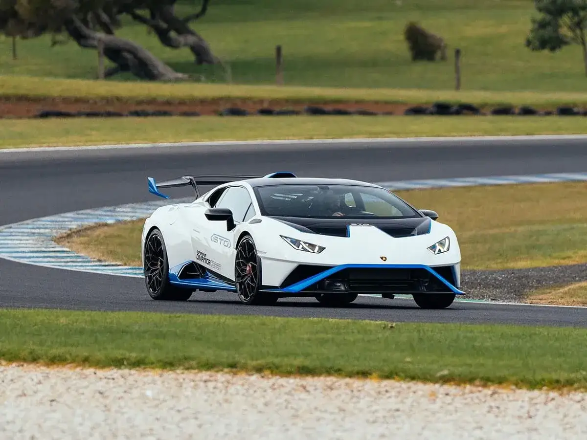 Biały Lamborghini Huracan STO z niebieskimi akcentami śmiga po torze wyścigowym, gotowy na każde wyzwanie.