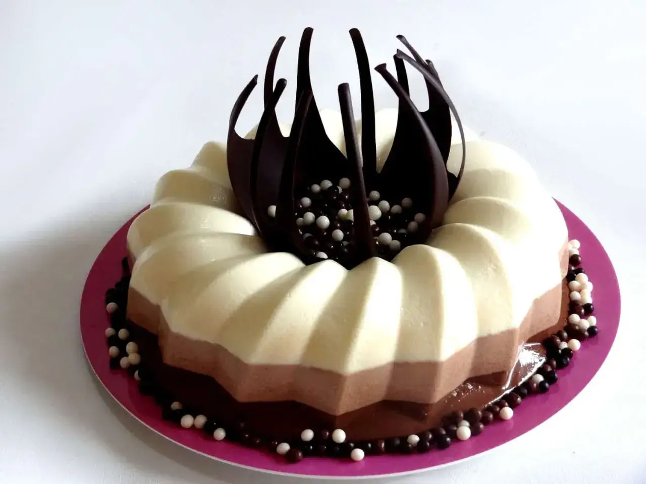 Tarta de tres chocolates con capas de blanco, con leche y negro, decorada con chocolate oscuro y bolitas.
