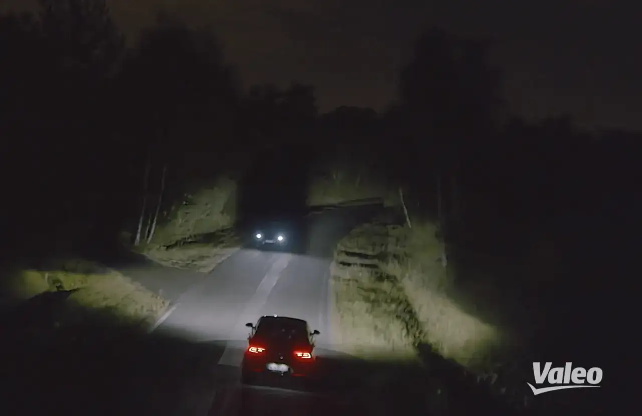 Dos coches circulan de noche por una carretera rural. Las luces adaptativas iluminan el camino, mostrando la seguridad y visibilidad que ofrecen.