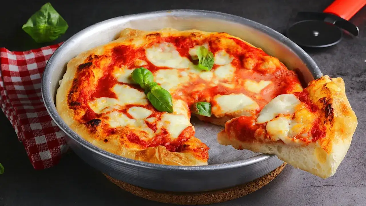 Pizza al padellino appena sfornata, con pomodoro filante e basilico fresco. Una fetta invitante si stacca dal bordo dorato.