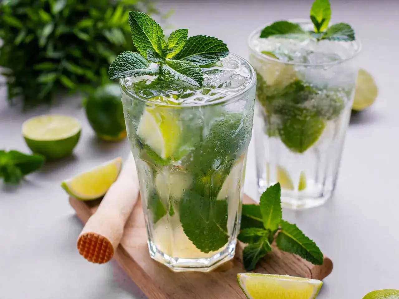 Erfrischendes Mojito-Rezept: Gl&auml;ser gef&uuml;llt mit Eis, Limettenst&uuml;cken und Minze. Ein M&ouml;rser liegt bereit.
