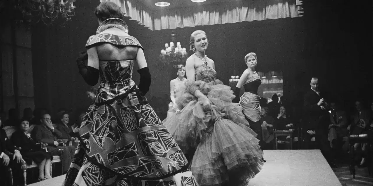 Desfile de alta costura, un momento clave en la historia de la moda. Modelos lucen vestidos voluminosos y estampados audaces ante un p&uacute;blico atento.