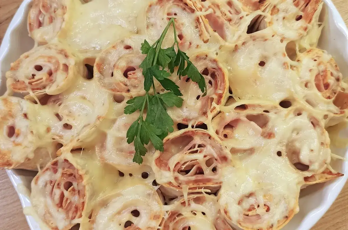 Roladki z tortilli z szynką i serem, zapieczone pod ciągnącym się serem, ozdobione gałązką natki pietruszki.