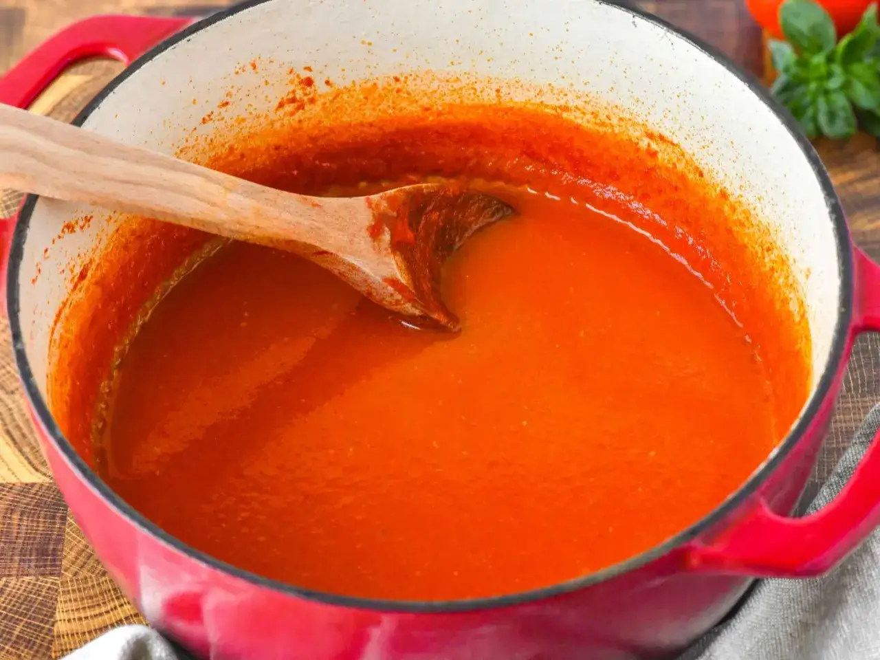 Ein hölzerner Löffel rührt in einem roten Topf mit köstlicher, frisch zubereiteter tomatensauce aus frischen tomaten.
