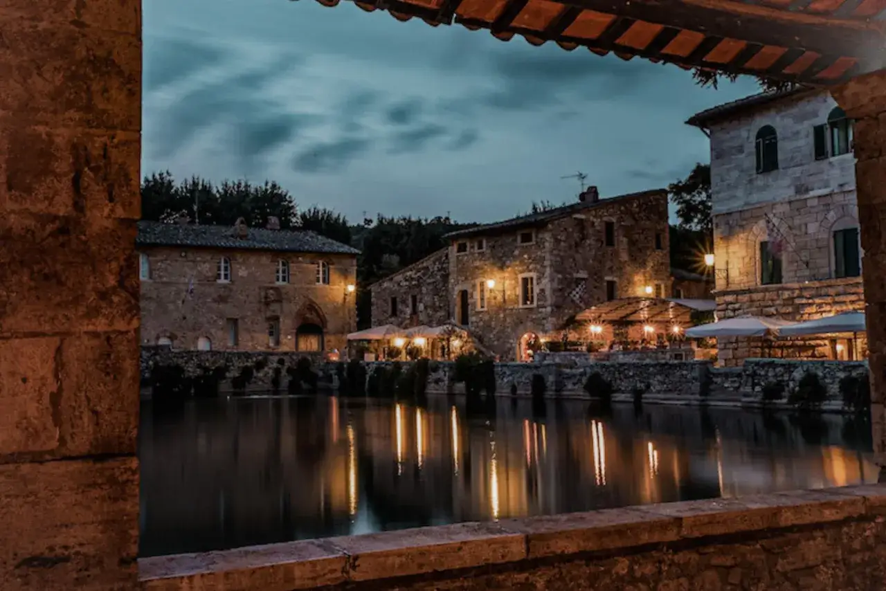 Un suggestivo **weekend nel centro Italia**: antichi borghi in pietra illuminati da luci calde si specchiano in un laghetto tranquillo.