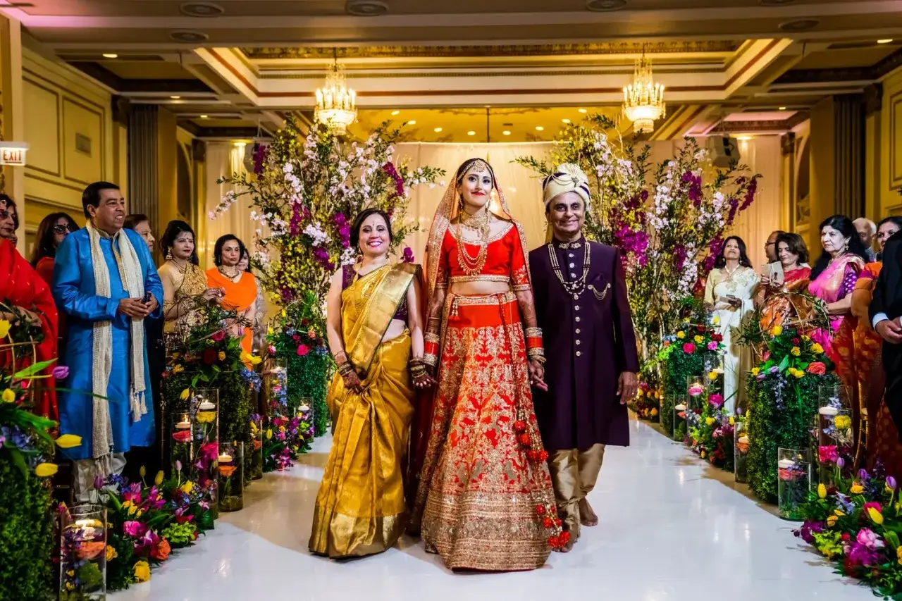 La mariée, accompagnée de ses parents, rayonne dans une tenue éclatante, un moment digne d'un mariage Bollywood.