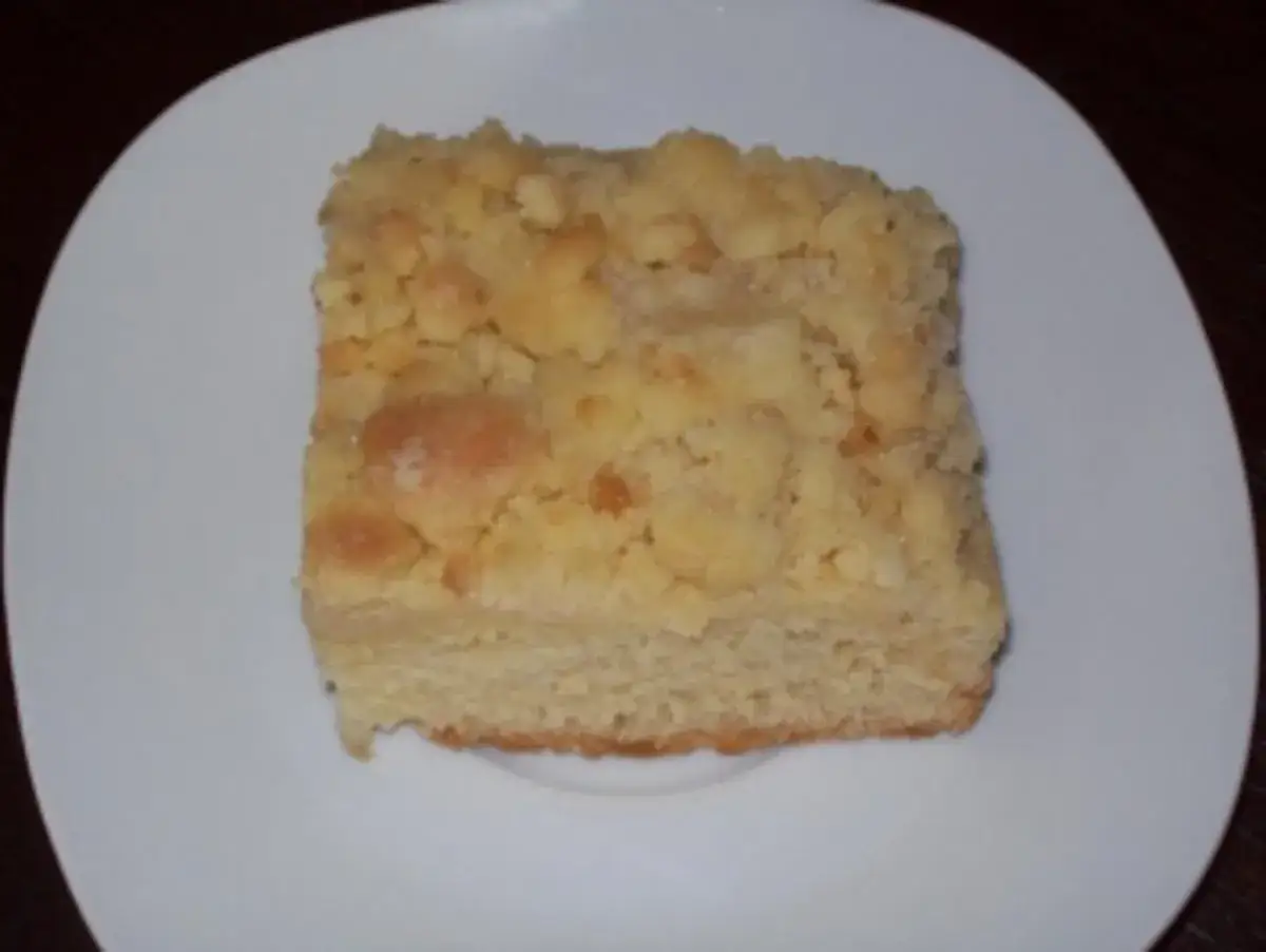 Ein Stück saftiger Streuselkuchen vom Blech auf einem weißen Teller.