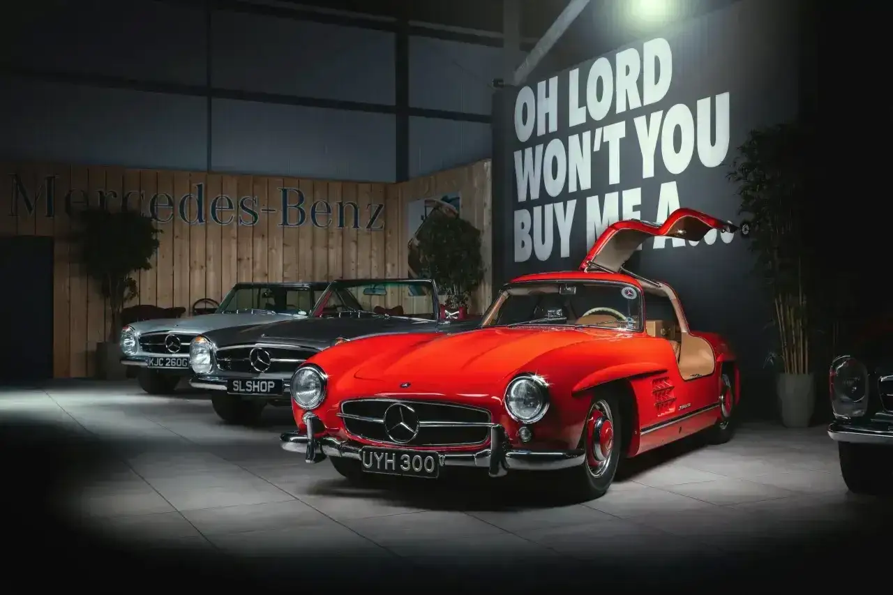 Czerwony Mercedes 300 z drzwiami skrzydłowymi, obok dwa inne klasyczne modele.