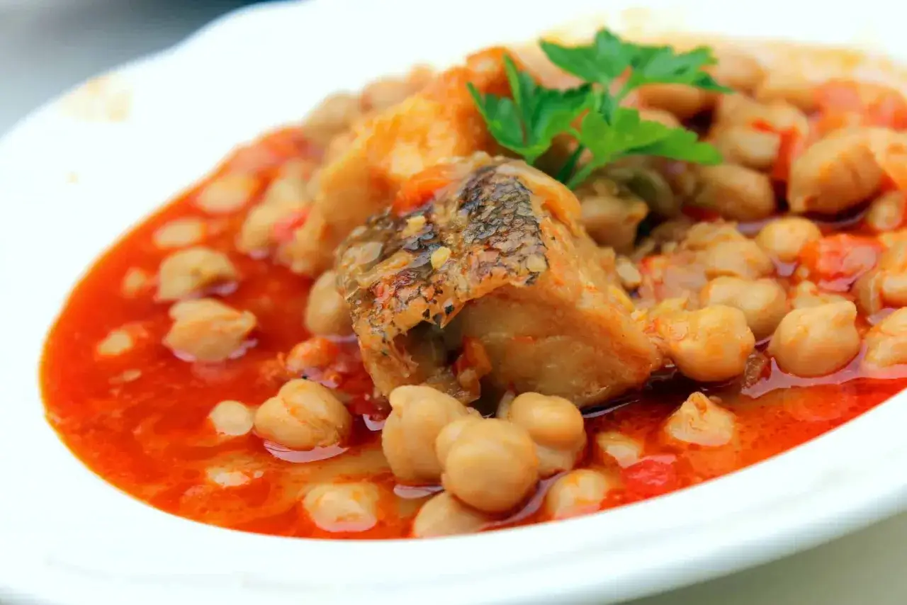 Un plato de garbanzos con trozos de pescado en salsa roja, una delicia que no te puedes perder si te preguntas qué comer en Cabo de Gata.