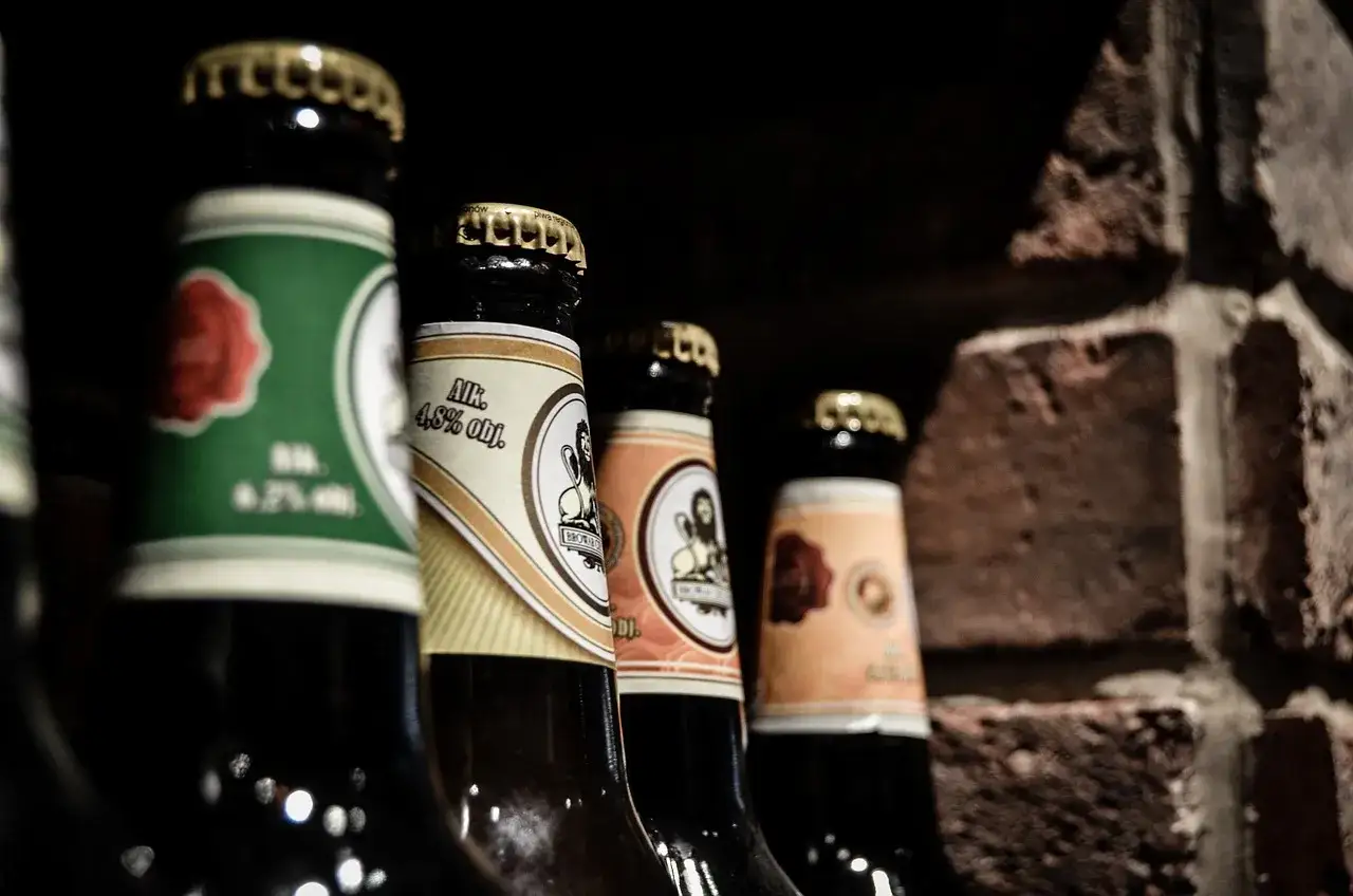 Butelki piwa w ciemnym wnętrzu, z widocznymi etykietami. Mogą to być objawy wygaśnięcia terminu przydatności piwa w puszce, choć tu mamy butelki.