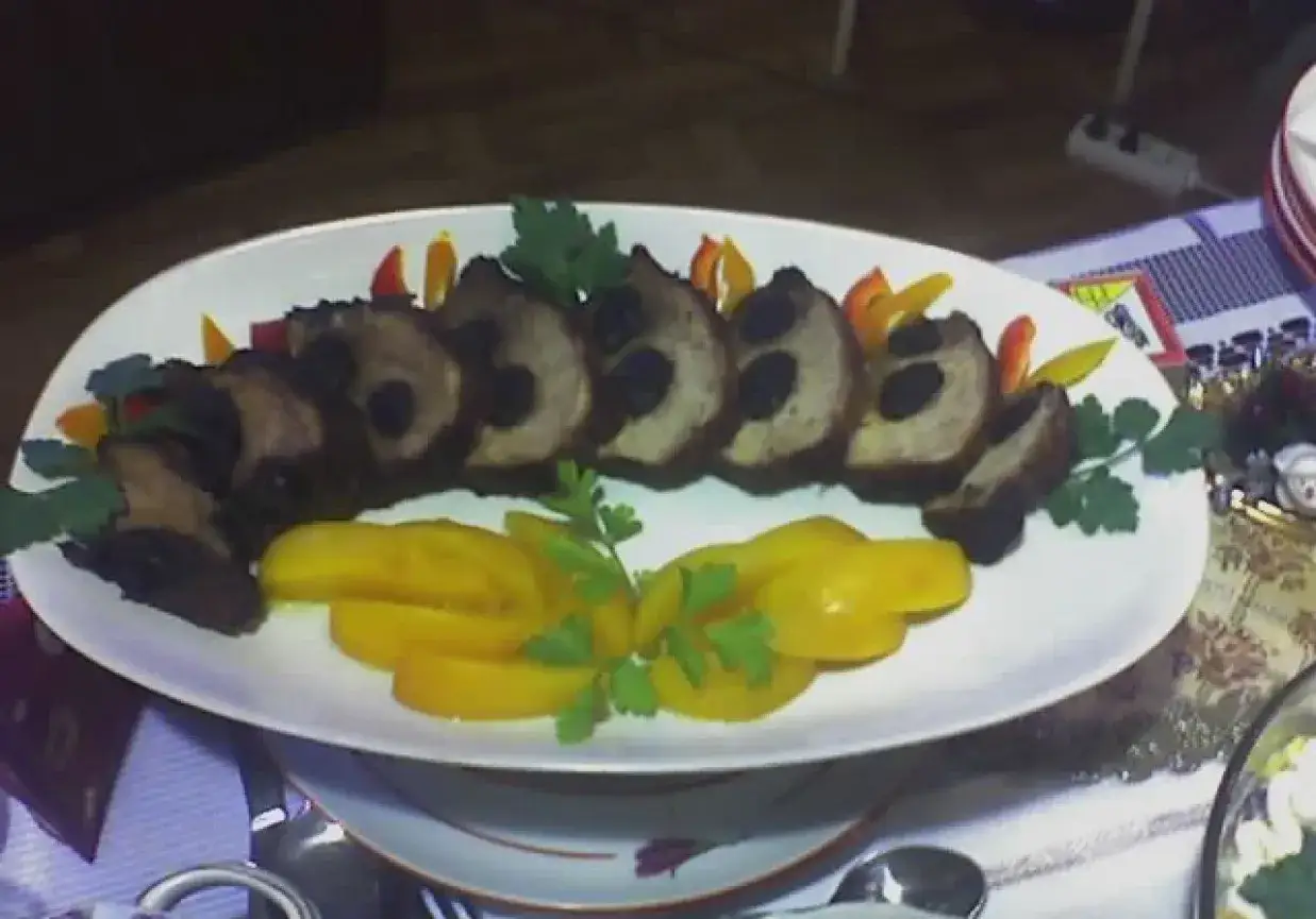 Apetyczna mięsna plata z plastrami mięsa nadziewanego oliwkami, ozdobiona papryką i natką pietruszki, podana z żółtymi warzywami.