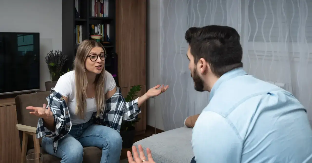 Kobieta z okularami gestykuluje, wyrażając frustrację w związku. Mężczyzna siedzi tyłem, słuchając jej.