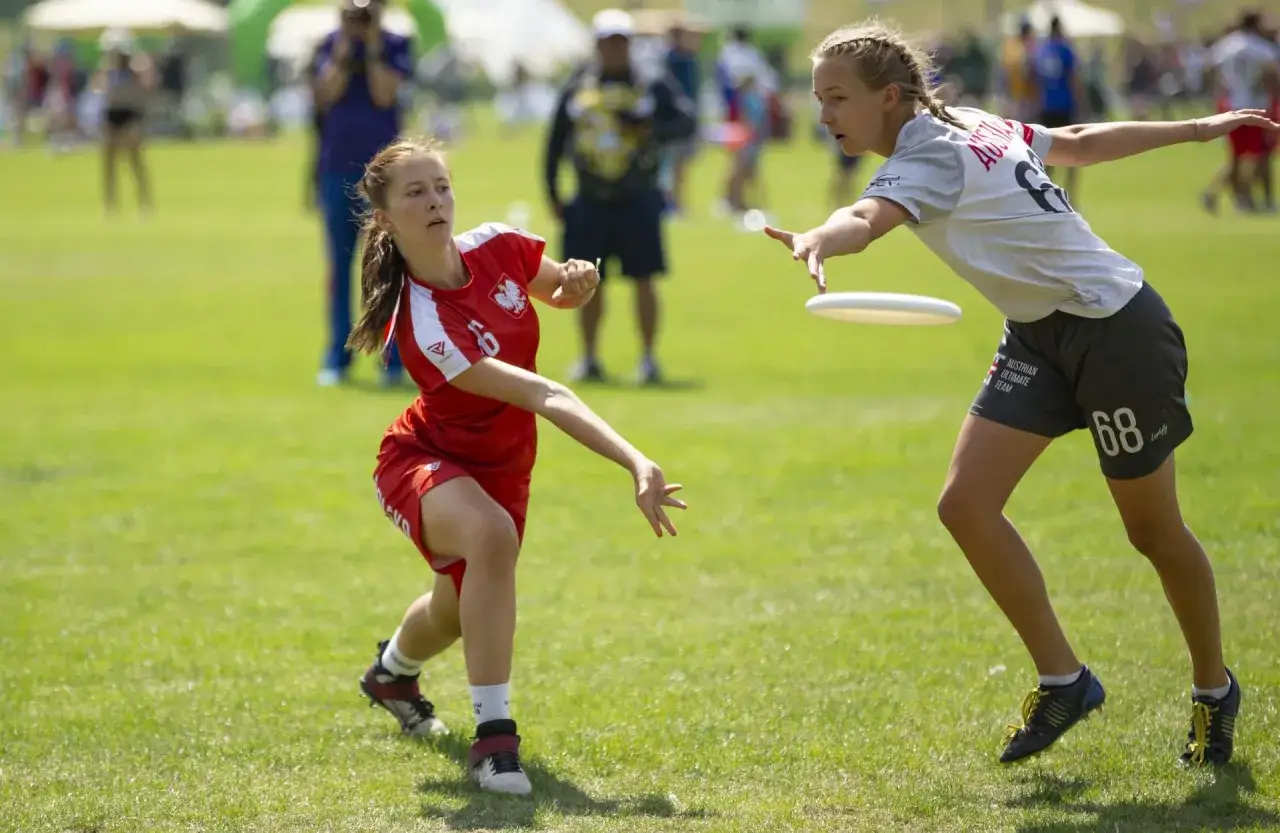 Dwie dziewczyny grają w ultimate frisbee, to świetne gry plenerowe dla młodzieży. Jedna rzuca dyskiem, druga próbuje go złapać.