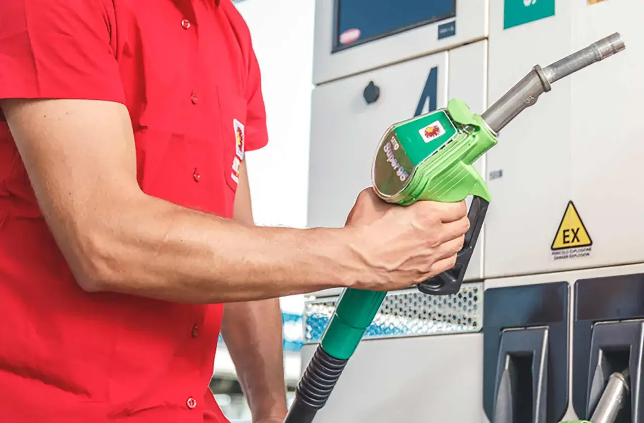 Un uomo in camicia rossa tiene una pistola erogatrice di benzina Super 95.