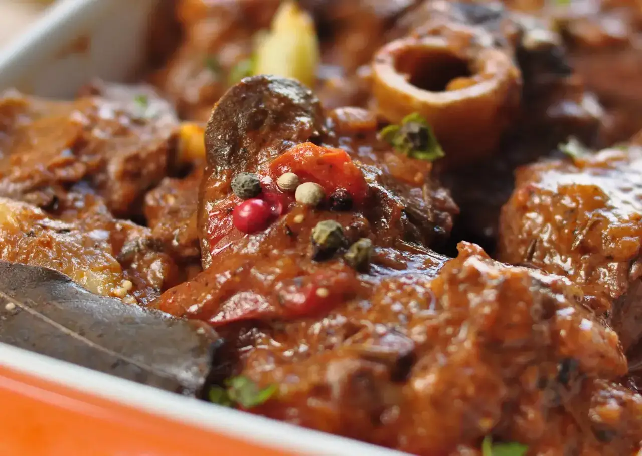 Guiso de carne con trozos de hueso, ba&ntilde;ado en una salsa rojiza y especiado con granos de pimienta y laurel. Un plato que evoca el sabor del ajo carretero.
