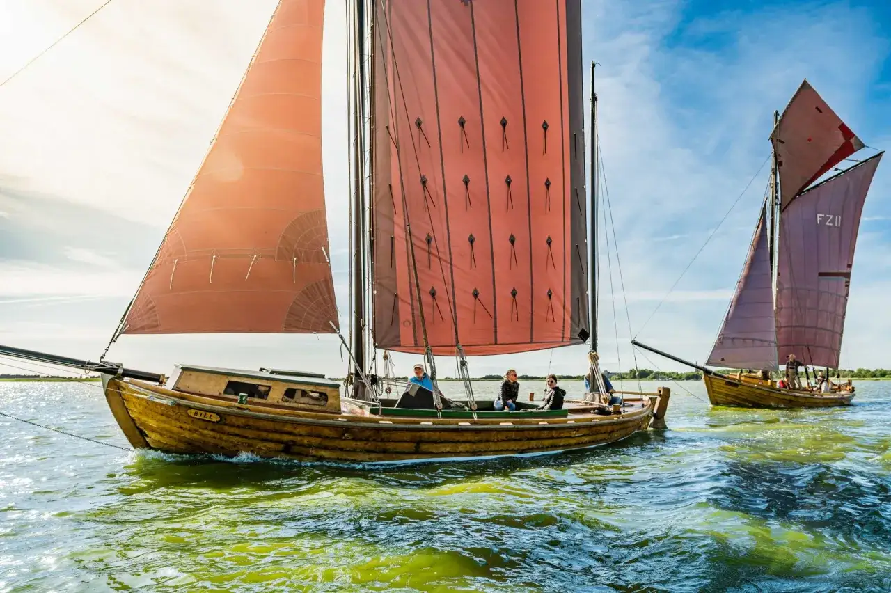 Zeesboot Ahrenshoop gleitet über das Wasser, rote Segel im Wind.