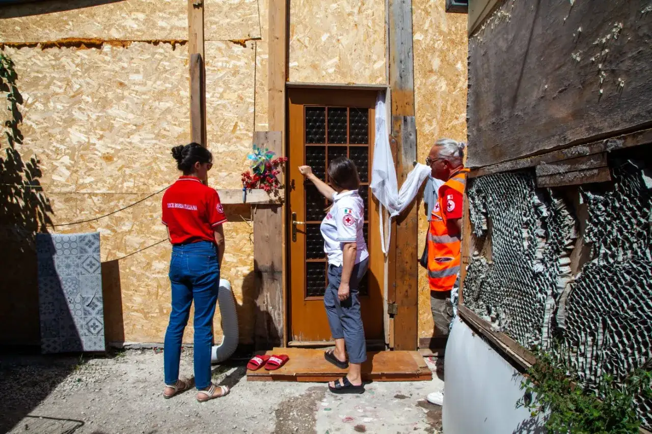Volontari della Croce Rossa Italiana al campo rom di Castel Romano, davanti a una porta di legno.