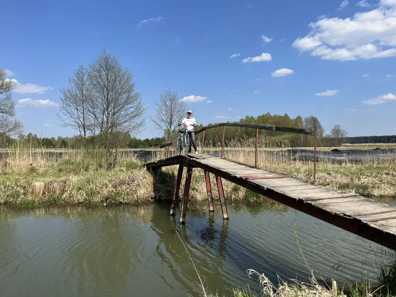 Osoba z rowerem na drewnianym moście nad rzeką, odkrywająca urokliwe trasy rowerowe łódzkie.
