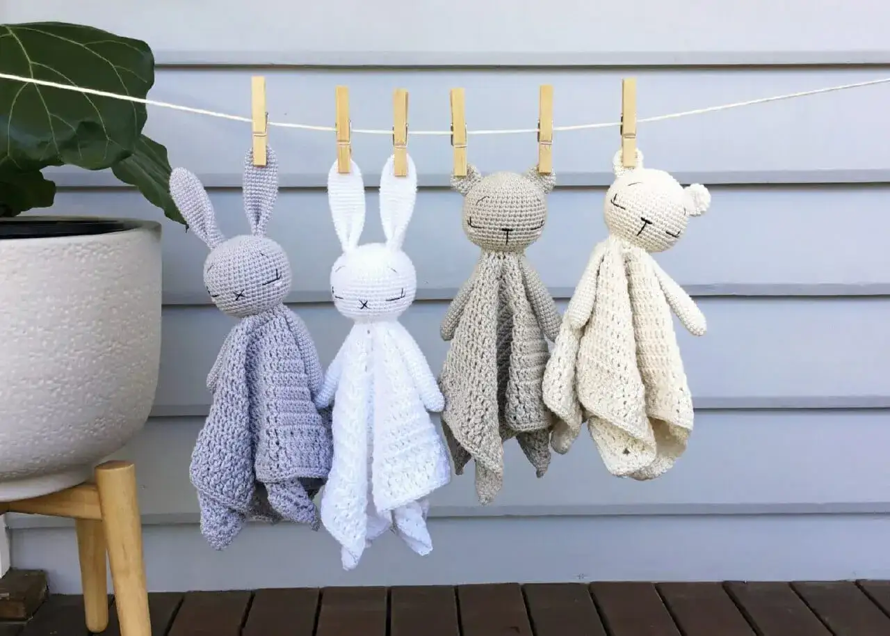 Cuatro adorables mantas de apego crochet, dos conejitos y dos ositos, cuelgan de una cuerda.