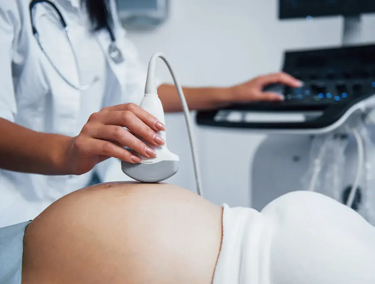 Ecografía de una mujer embarazada, capturando los primeros pasos del embarazo. La mano de la doctora sostiene el transductor sobre el vientre.