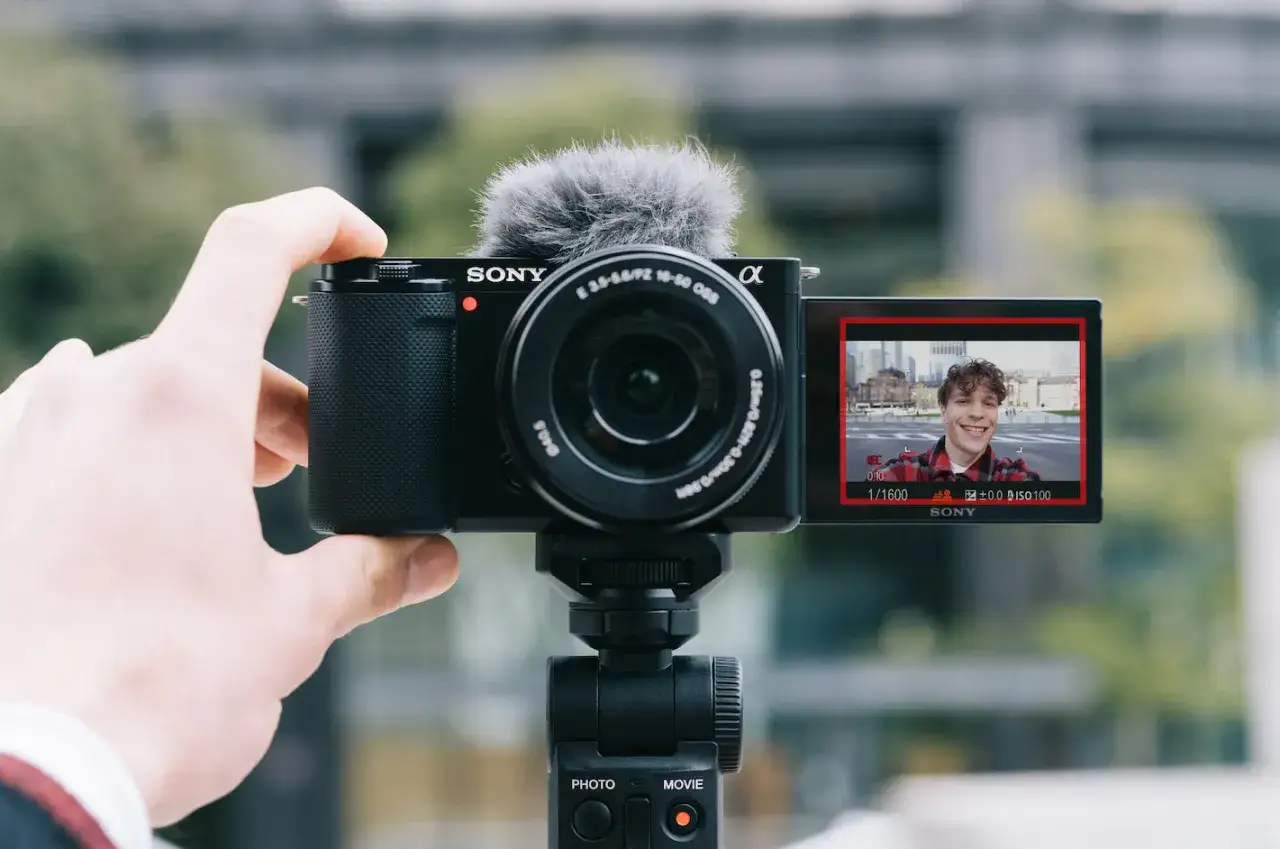 Mężczyzna nagrywa siebie na kamerze Sony zve10. Uśmiechnięty vloger w kratę na ekranie.