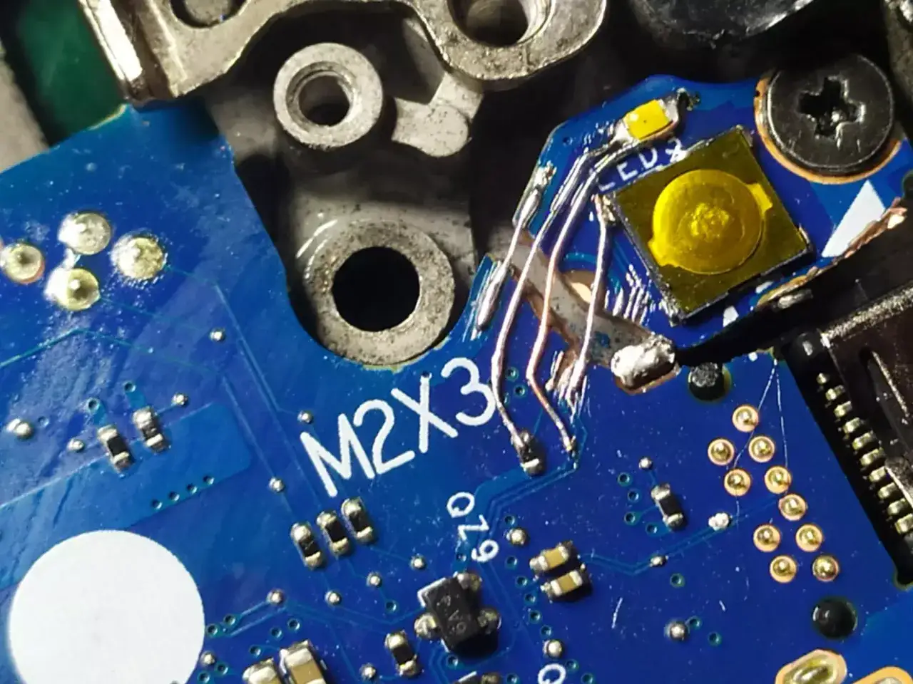 Naprawa ścieżki na płytce M2X3 za pomocą drucik&oacute;w. Widoczne elementy elektroniczne i lutowanie.