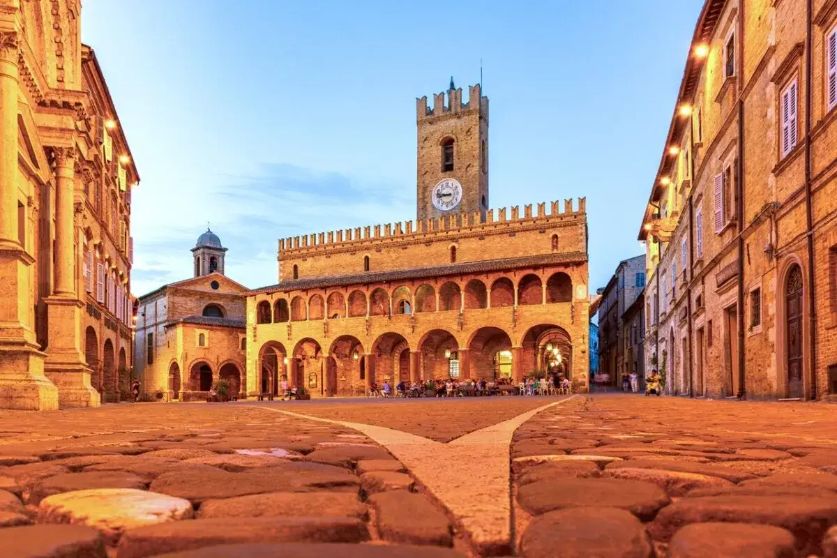 Piazza del Popolo a Ripatransone, un gioiello per un itinerario Marche 5 giorni. Edifici storici illuminati, torre con orologio e ciottoli antichi.
