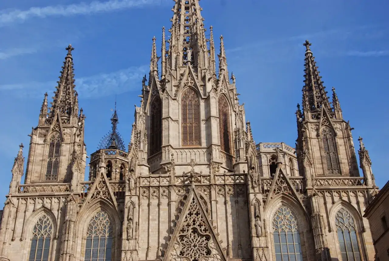Detalle de la Catedral de Barcelona, con sus impresionantes contrafuertes y arbotantes góticos que se elevan hacia el cielo azul.
