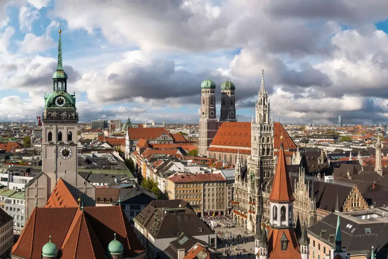Monachium ciekawostki: widok na Frauenkirche, wieżę ratuszową i inne zabytki miasta pod zachmurzonym niebem.