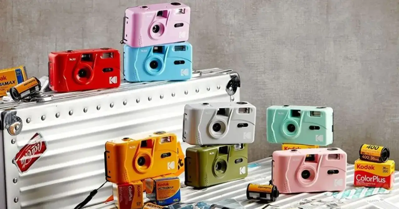 Kolorowe aparaty Kodak M35 w pastelowych barwach: różowy, niebieski, czerwony, żółty, zielony, biały i miętowy, ułożone na walizce.