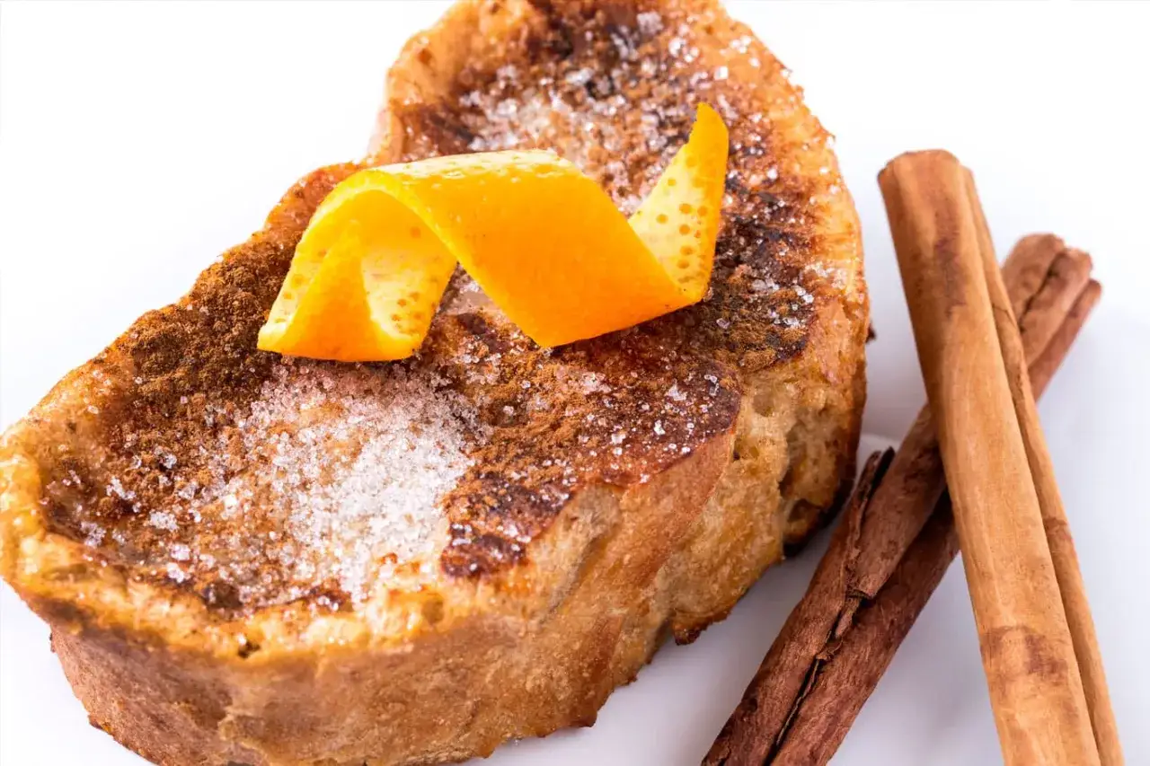 Torrijas de vino espolvoreadas con azúcar y canela, decoradas con piel de naranja y acompañadas de ramas de canela.