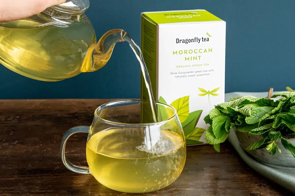 Zaparzona zielona herbata miętowa, idealna na odchudzanie. Obok pudełko herbaty Dragonfly Tea Moroccan Mint i świeża mięta.