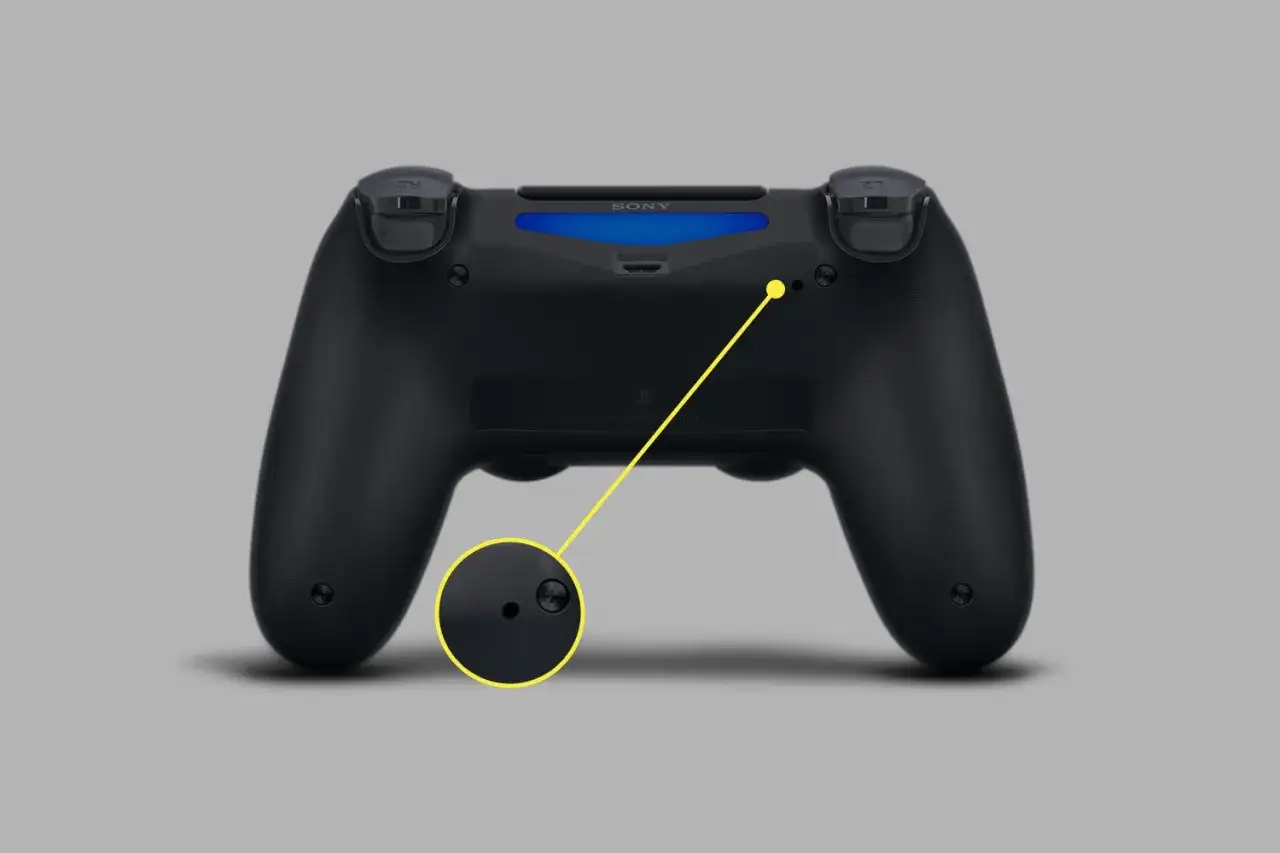 Czarny pad PS4 z widocznym przyciskiem resetowania. Dowiedz się, jak zresetować pada PS4, naciskając ten mały otw&oacute;r.