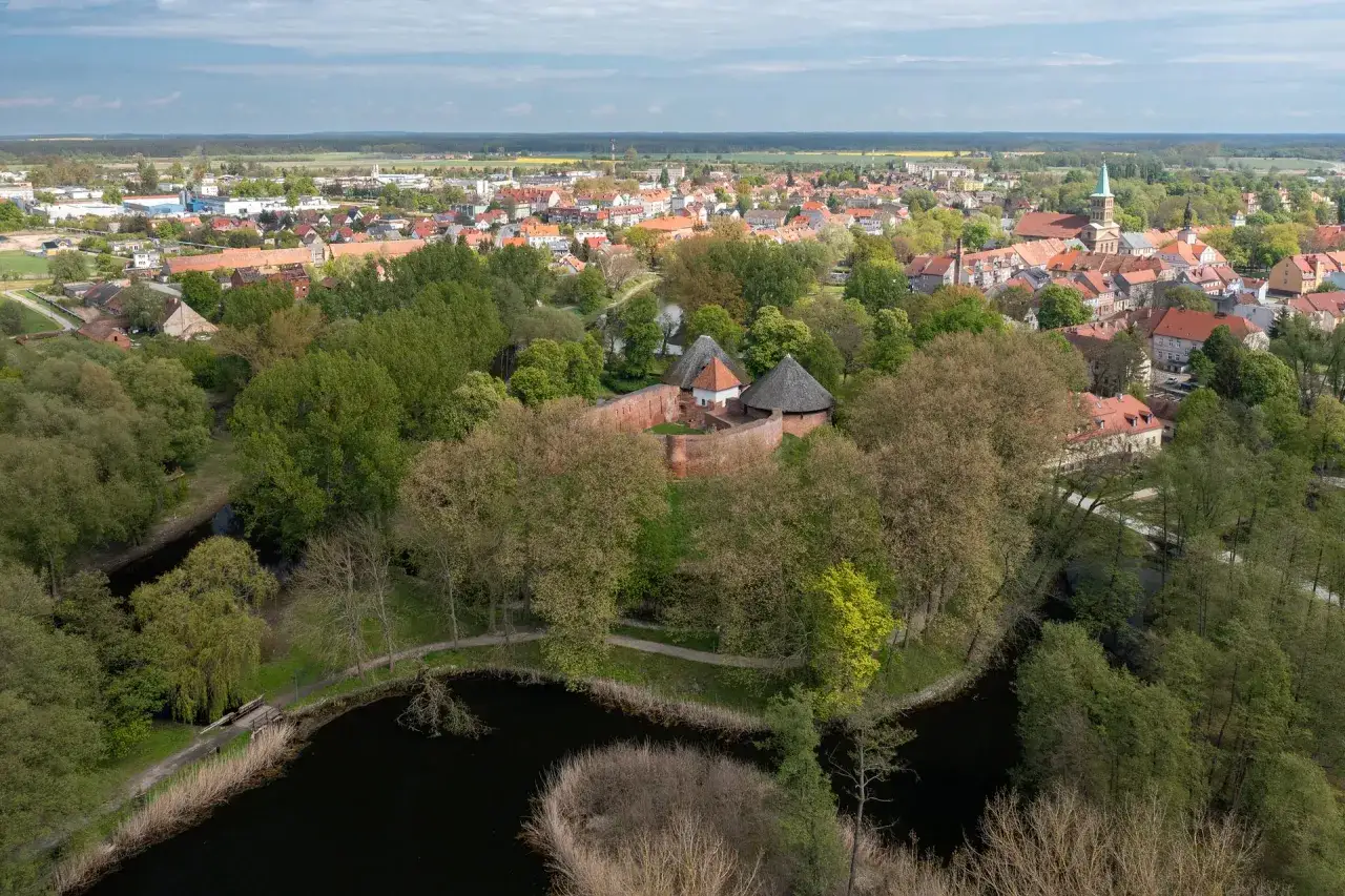 Zamek międzyrzecz otoczony zielenią, z widokiem na miasto i kościół.
