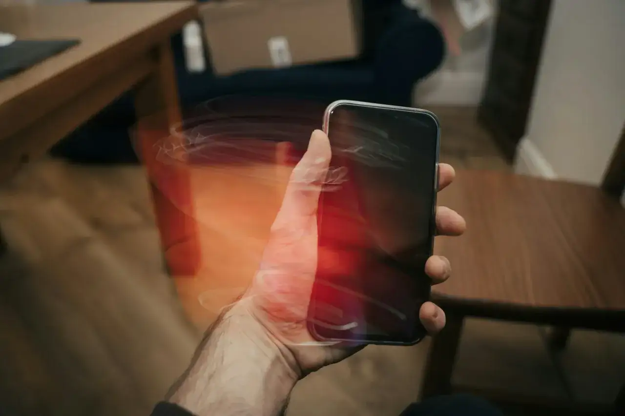 Dłoń trzyma smartfon, który wiruje, tworząc świetlne smugi. W tle widać meble i kartonowe pudło.