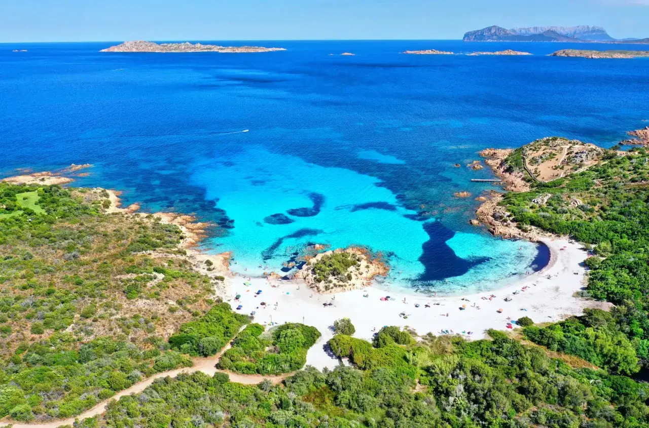 Spiaggia bianca e acque cristalline nel **mare della Sardegna**, con rocce e macchia mediterranea.