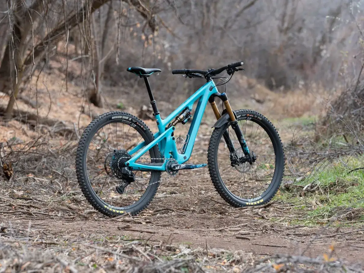 A turquoise Yeti SB140 mountain bike rests on a dirt trail, ready for adventure in the woods.