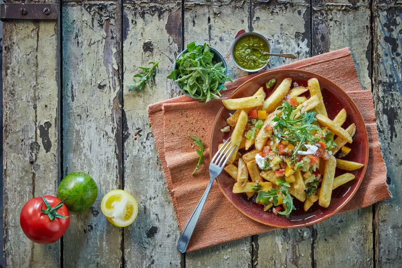 Pyszne frytki jak z maka, podane z salsą, rukolą i sosem pesto na rustykalnym stole.